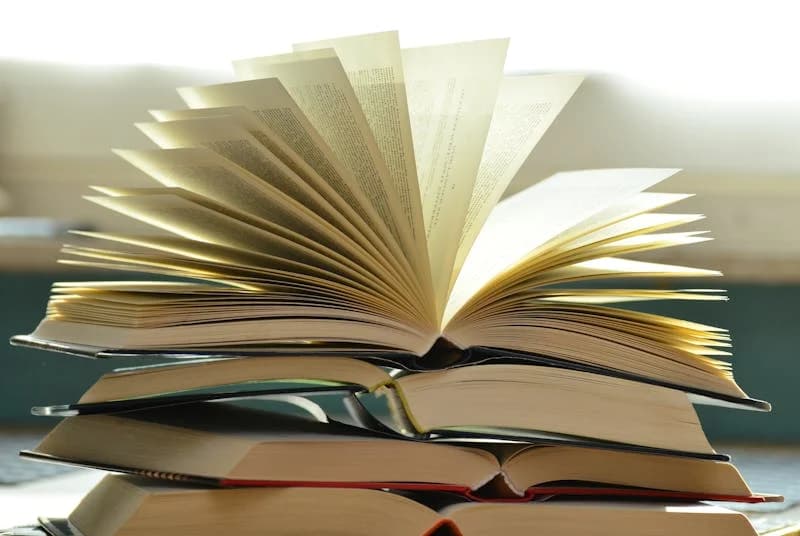 A stack of open books, the topmost of which has its pages fanned out.