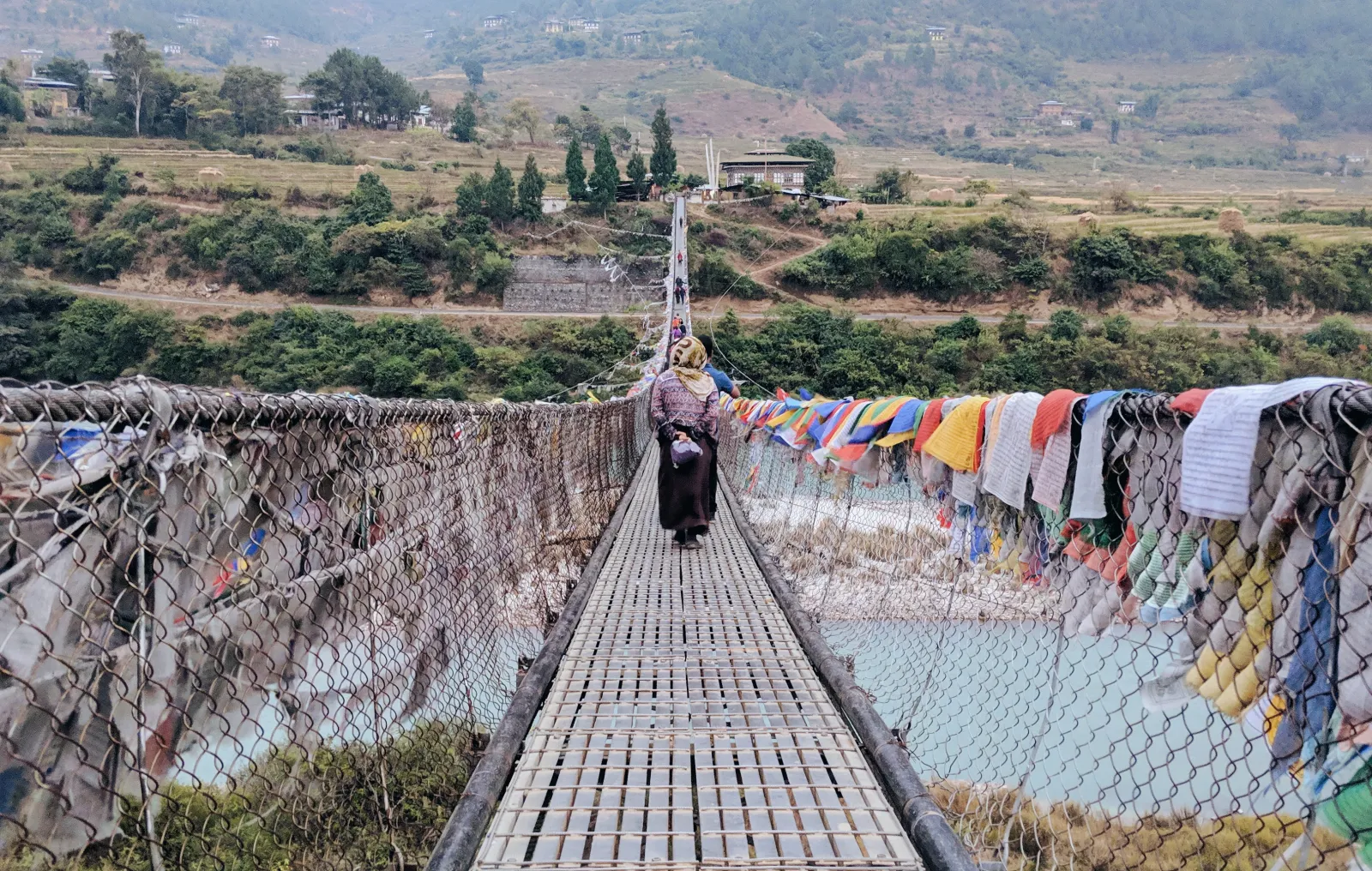 A long suspension footbridge strung with prayer flags across a Bhutanese valley