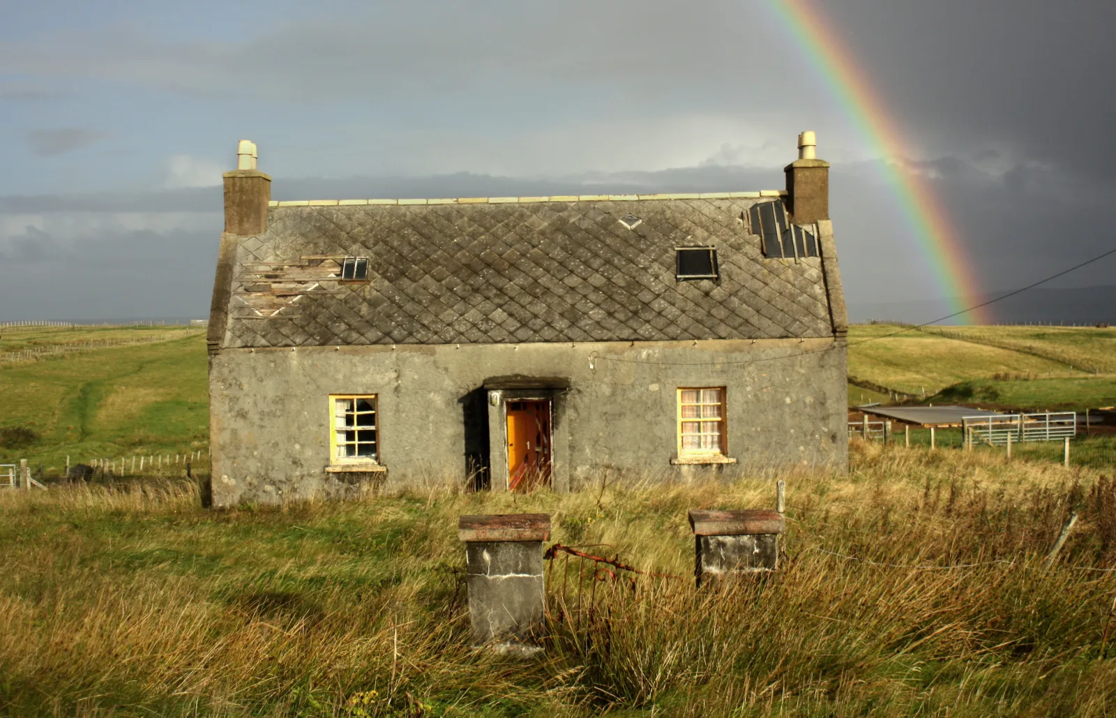 A stone croft cottage on open moorland beneath a rainbow