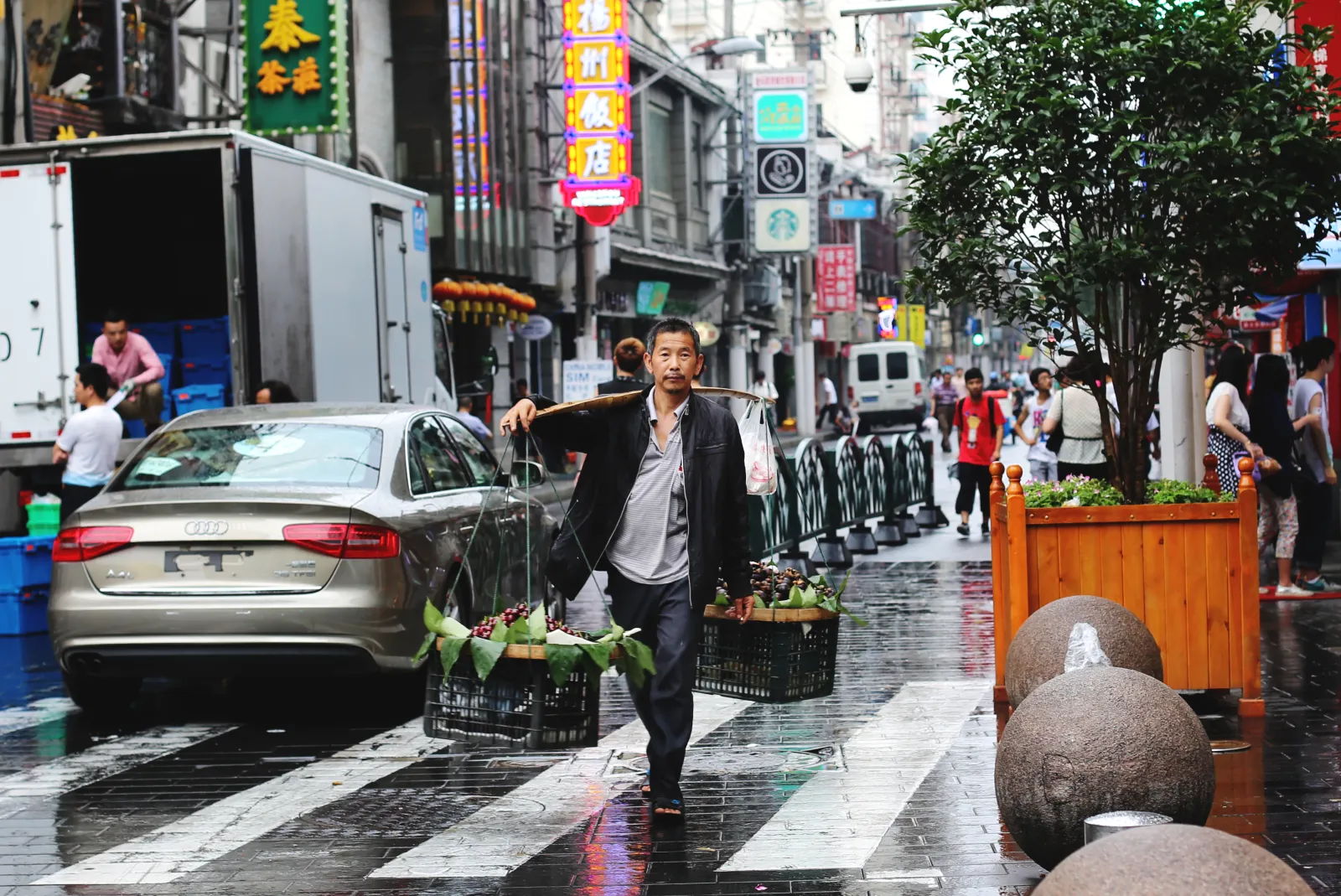 A Shanghai street in the rain, shopfronts and traffic behind a man walking