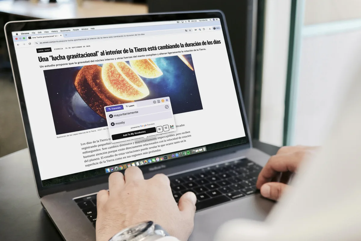 A person typing on a laptop showing a Spanish news article, with the Mango Reader popup translating the word “mayoritariamente” as “mostly”.
