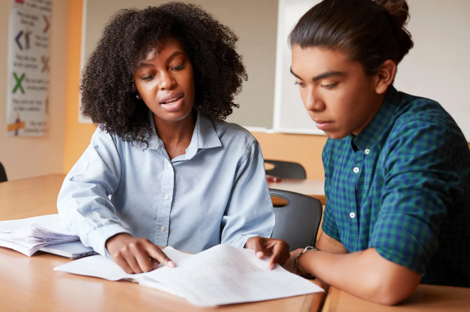 A teacher and a teenage student working through a worksheet together at a desk.